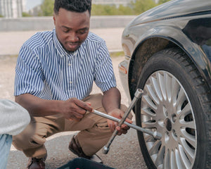 Person changing a flat tire safely on the side of the road using a lug wrench