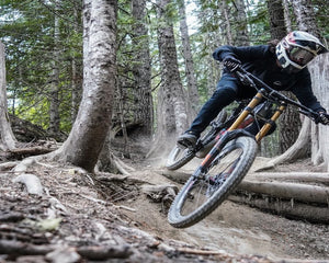 Mountain biker riding trail through forest showing terrain where tubeless vs tubed tire choice matters